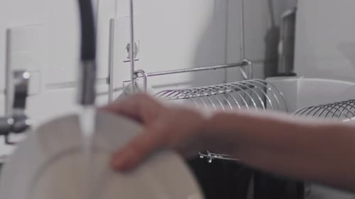 Stacking ceramic plate on kitchen drying rack after washing under water tap. Slow motion