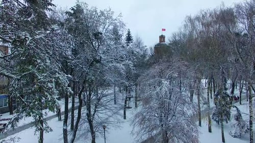 Park in winter season with old tower with clock. Drone rising over the snowy city panorama