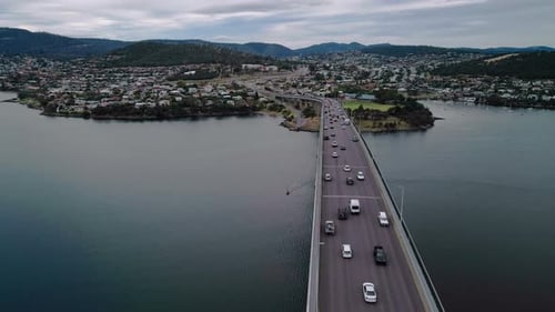 Vue aérienne d'un pont sur lequel circulent des véhicules par temps nuageux avec un paysage urbain en arrière-plan.