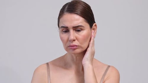 Mujer reflexiva, triste, deprimida, preocupada, de mediana edad, 40-44 años, sobre fondo gris