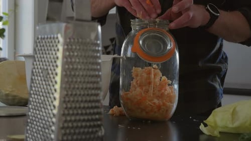 Person Pouring carrots and cabbage mixture in glass jar, ready to fermentation process, Kombucha Dri