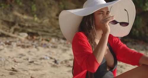 Latin Girl Model Casually Sits Up to put Sunglasses on whilst Suntanning on Beach in Bright Sunshine
