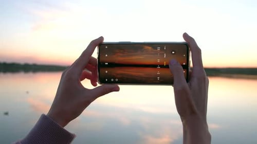 Hands of Woman Taking Photo with Phone of Sunset in Summer Day