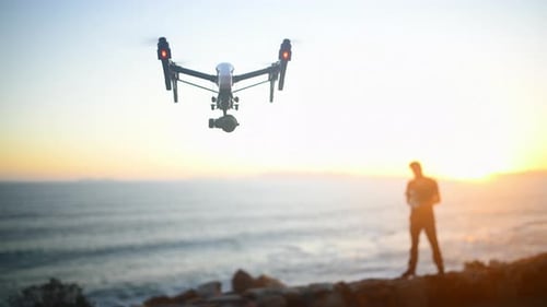 Beach, blurred background and a man flying a drone over the ocean in nature for video footage during