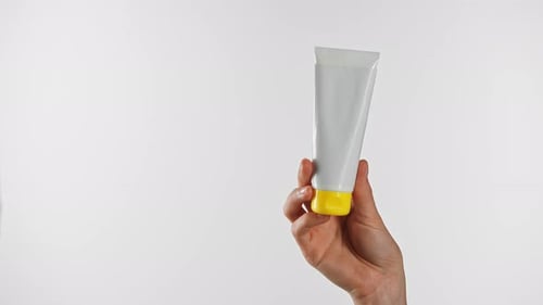 White Tube with Yellow Cap Held By Hand