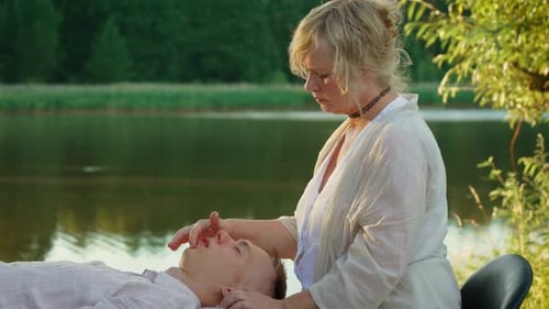 Massagista trabalhando suavemente na cabeça perto de um tranquilo terapeuta fluvial com foco no relaxamento cercado por