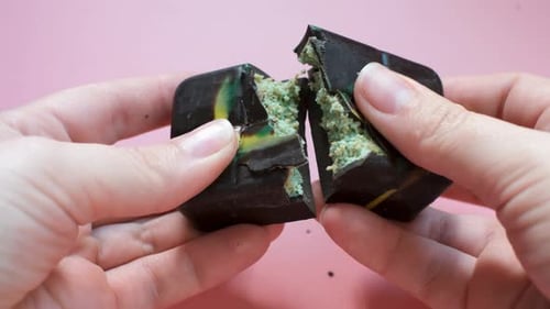 Female hands breaking a piece of Dubai chocolate top view on pink background.