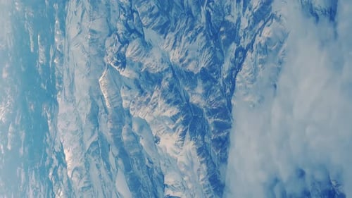 Wing of Flying Above Soft Fluffy Clouds and Snowy Mountains Airplane As Seen By Passenger Through