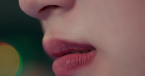 Une femme porte les lèvres et les mord en les suçant avec des lumières bokeh derrière elle, plan détaillé