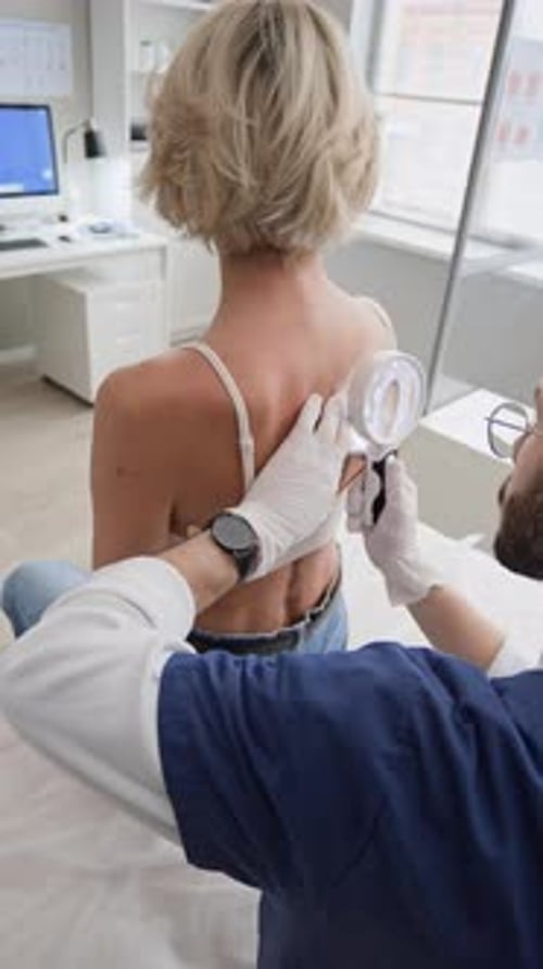 Dermatologist Using Magnifying Glass while Examining Back of Female Patient