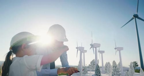 A father engineer shows his project to his daughter for the construction of a wind farm. The daugh