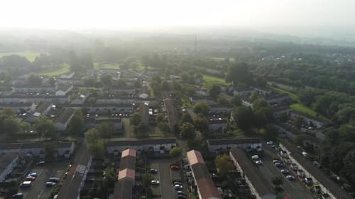 Elevated aerial view over residential British town houses during hazy golden hour pan right