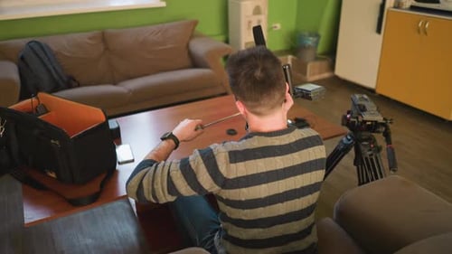 Back Shot of Studio Guy Adjusting Camera Lens on Tripod Preparing for Video Shoot