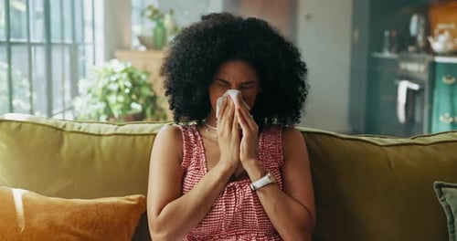 Mujer, estornuda y pañuelos de papel en el sofá de la casa, enferma y con sinusitis con gripe, alergia