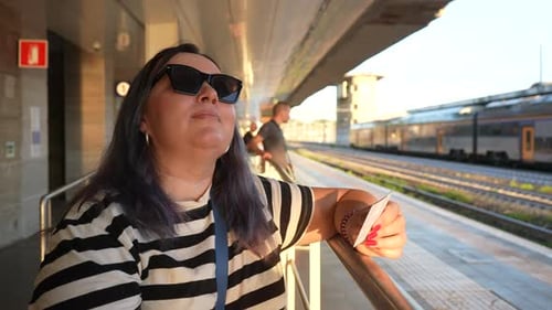 Closeup Portrait of Happy Female Traveler in Sunglasses Looking at Ticket While Standing Waiting for