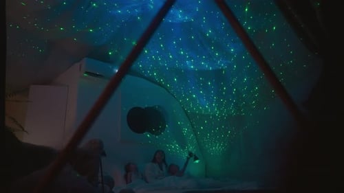 Mom with Kids Lies on Bed Under Projection of Sky on Ceiling