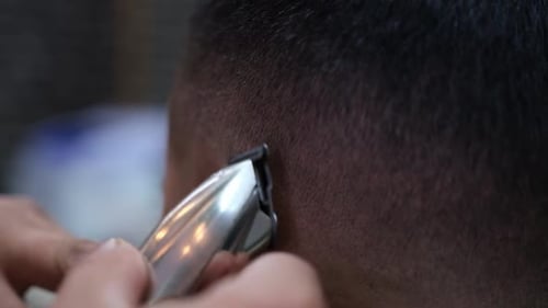 Extreme close-up of a barber using an electric razor to give a male customer a very short cut.
