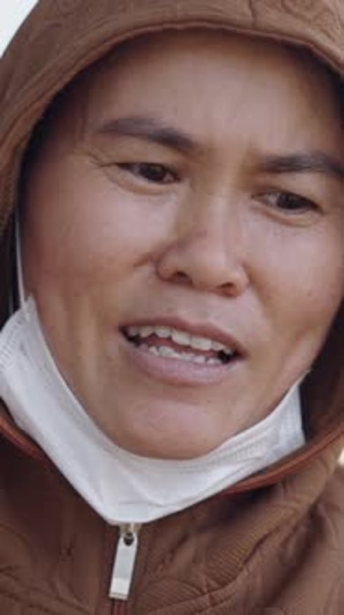 Retrato de una joven asiática con máscara facial en el cuello saludando a la cámara con los dedos en forma de V