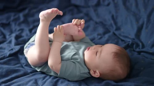 Adorable Caucasian toddler lies on his back on the bed.