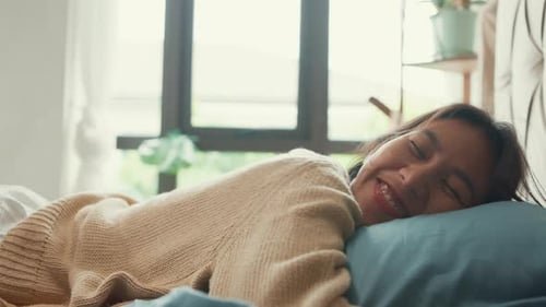 Close-up Asian girl with white cream pajamas lay head down on pillow close eyes happy smiling feel.