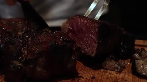 Fork and knife carve delicious thick juicy cooked rare steaks on wooden chopping block, close up