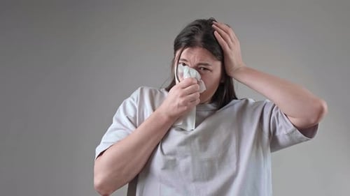 Joven morena cierra los ojos y se suena la nariz, lidiando con la congestión nasal de temporada