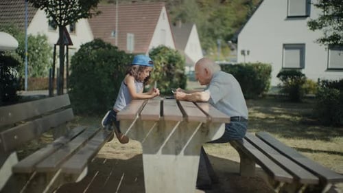 Opa and granddaughter playing cards in a city park, Total shot