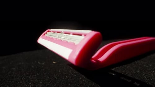 Pink disposable razor and stuck hair, on a black background. Dolly slider extreme close-up.