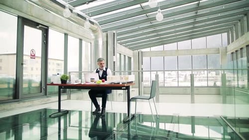 Reifer Architekt mit Laptop und Modell eines Hauses im Büro, bei der Arbeit.