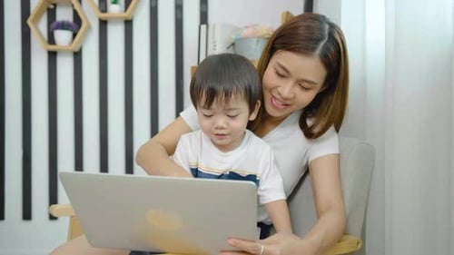 Young asian mother her little son using laptop enjoying watching funny social media video