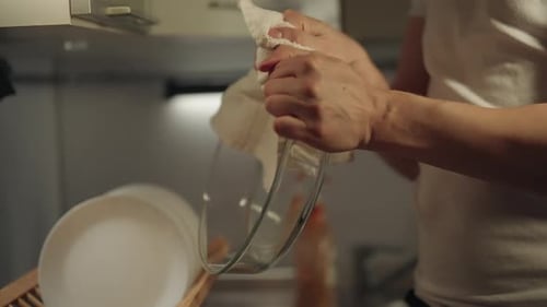 Cropped Shot of Man Drying Glass Bowl with White Cloth in Modern Kitchen Surrounded By Other Clean