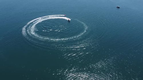 Motorboat spins tourists on tow raft around in circles, sunny aerial