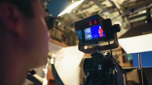 Cameraman Monitoring Presenter on Blue Screen During Studio Shoot with Lighting Gear