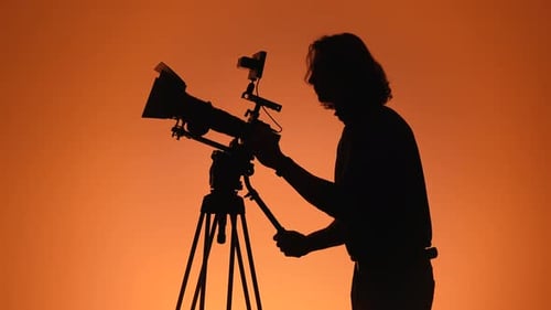 Silhouette of a Cameraman Adjusting Professional Equipment