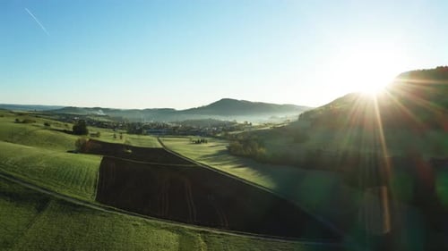 aerial drone view of morning hour over peaceful countryside with green and agricultural fields, path