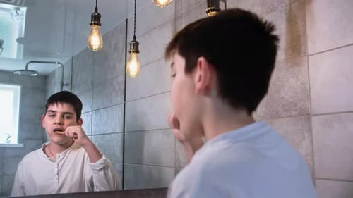 Niño adorable cepillándose los dientes con un cepillo de dientes de bambú y pasta mirándose al espejo en el baño