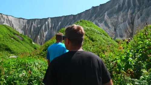 Group of people walks along hiking trail with rocks in summer.