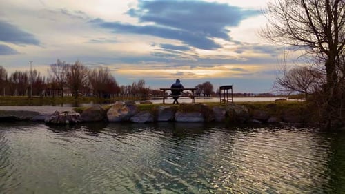 Man Fishing Alone By The Lake At Sunset