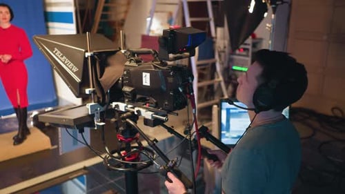 Cameraman Operating Camera While Filming Presenter in Studio with Blue Screen