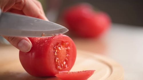 Woman cutting fresh tomato with a kitchen knife.