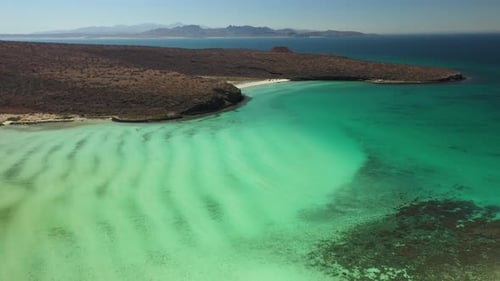 Cinematic drone shot of Balandra Beach, passing over the red hills and turquoise waters, wide reveal