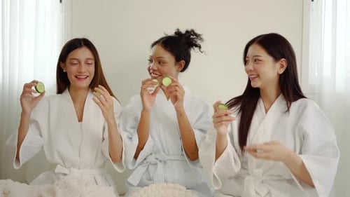 Three joyful young women wear cucumber masks over their eyes, laughing and enjoying each other
