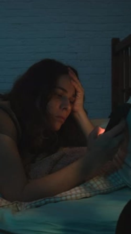 Vidéo verticale : femme insomniaque utilisant un téléphone portable allongée sur son lit la nuit