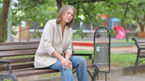 Mulher idosa com dor no joelho sentada no banco