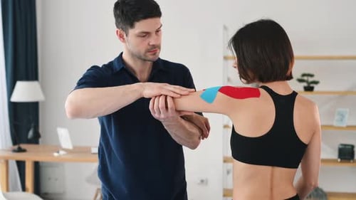 Man putting kinesio tape. Professional physiotherapist working with female customer