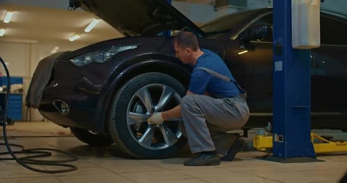 Auto Mechanic Screws a Car Wheel at a Service Station