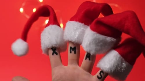 Fingers Dressed in SantaClaus Redwhite Hats and Word Text XMAS on Red Background Concept of