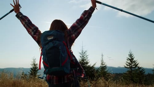 Excited woman hiker raising hands in air celebrating freedom in beautiful mountains