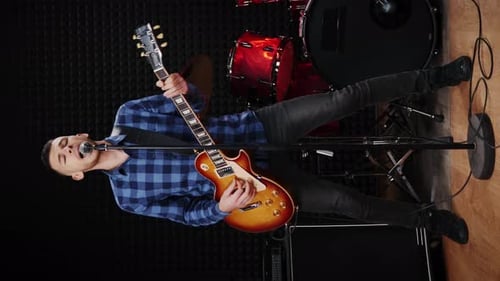 Musician singing song and playing on electric guitar at studio. Vertical video