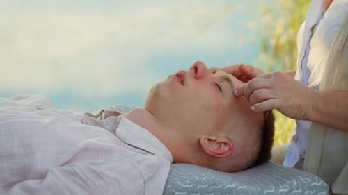 Terapeuta massageando a têmpora masculina perto da água, relaxando, melhorando a harmonia na natureza. Terapia calmante